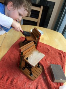 Little boy sanding and painting oil onto old school-desk bookends.